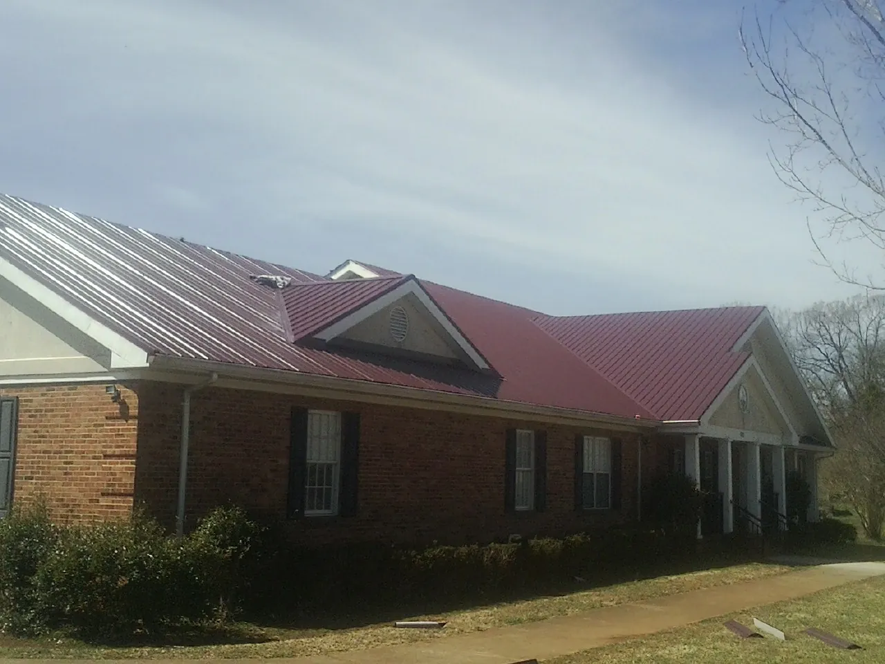 Red metal roof with gabled entries on a long brick building, from a Hail Damage Roof Repair job in Edwall
