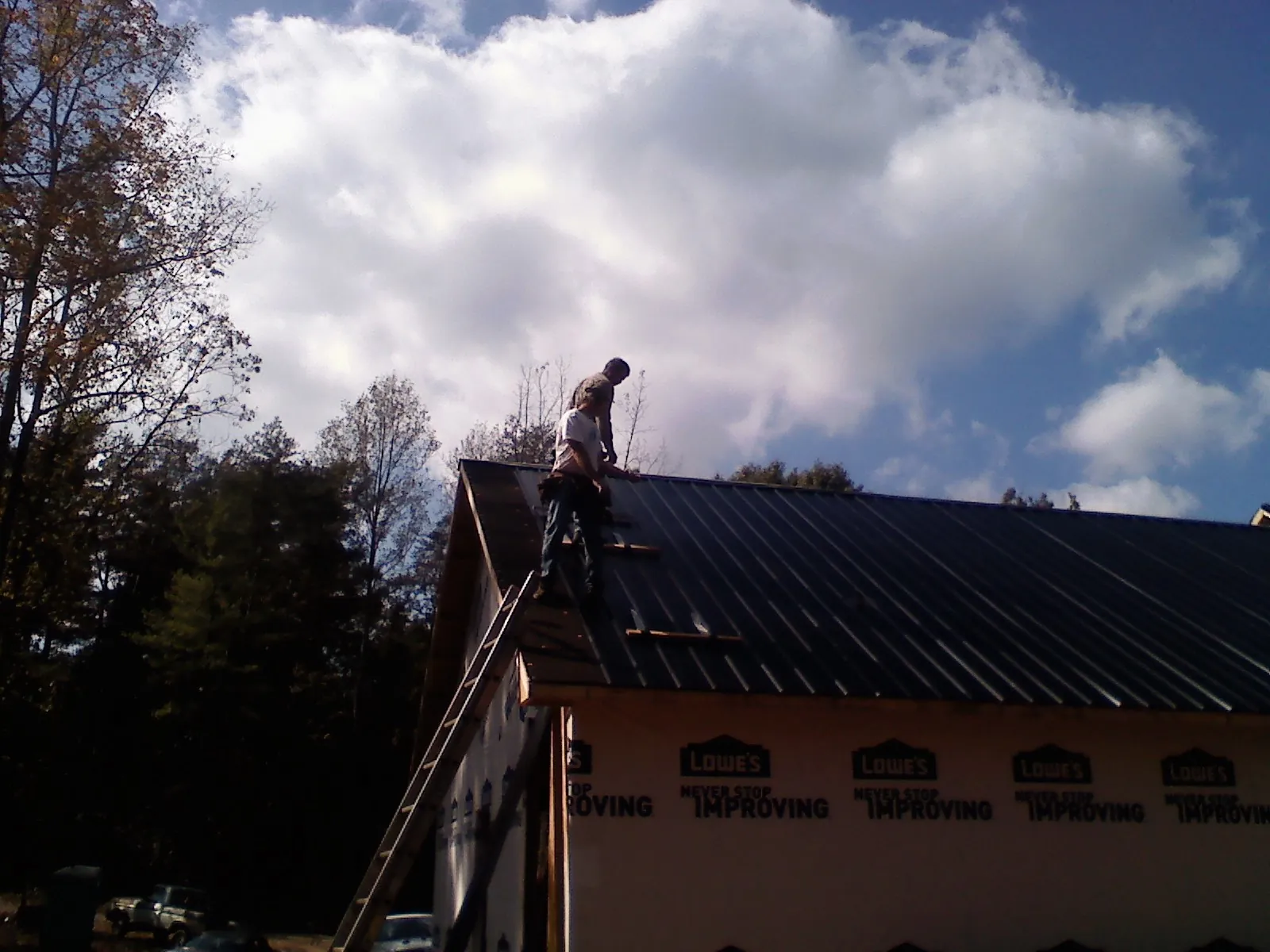 Roofer fastening dark metal panels high against a cloudy sky, from a Roof Inspection job in Edwall